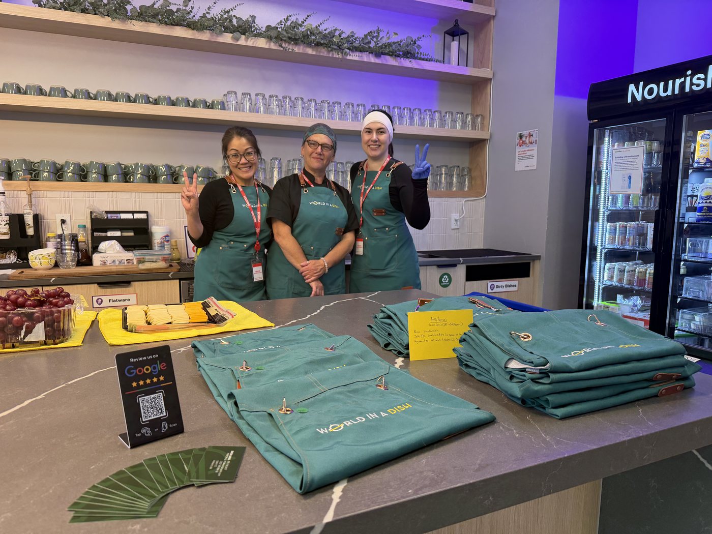 World in a Dish aprons folded on a counter beside the team, ready for guests to join in