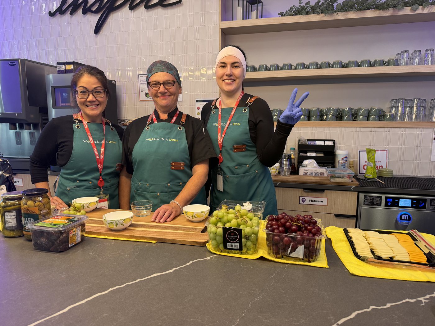 Three World in a Dish chefs in branded aprons behind a prep counter at an off-site team event